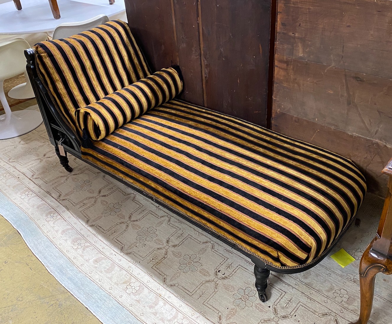 An Aesthetic period ebonised chaise longue, in the manner of E. W. Godwin, length 164cms, depth 61cms, height 75cms.